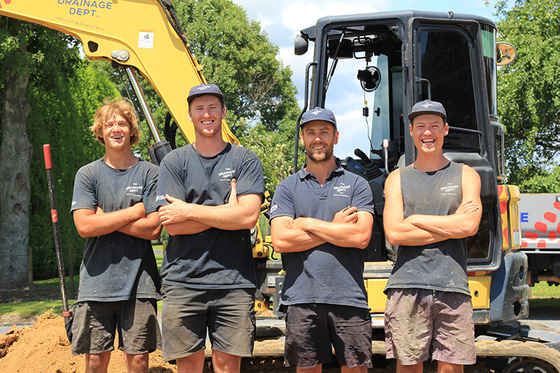 Four apprentices standing with their arms crossed in front of a digger